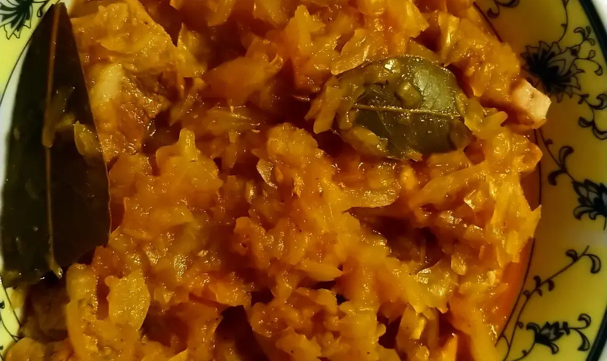 Pyszny bigos ze słodkiej kapusty z liściem laurowym, podany w żółtej misce z czarnym wzorem.