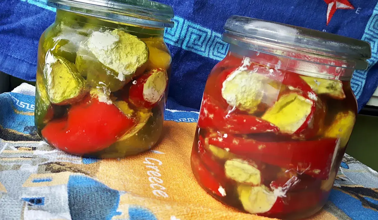 Dwa słoiki marynowanych papryczek nadziewanych serem feta na zimę. Papryczki w zalewie z oliwy i przypraw.