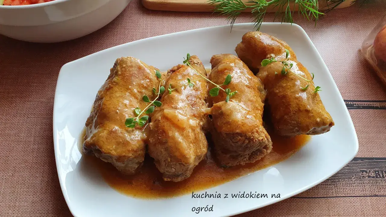 Roladki z karkówki w sosie, udekorowane gałązkami tymianku, obok miski z sałatką.