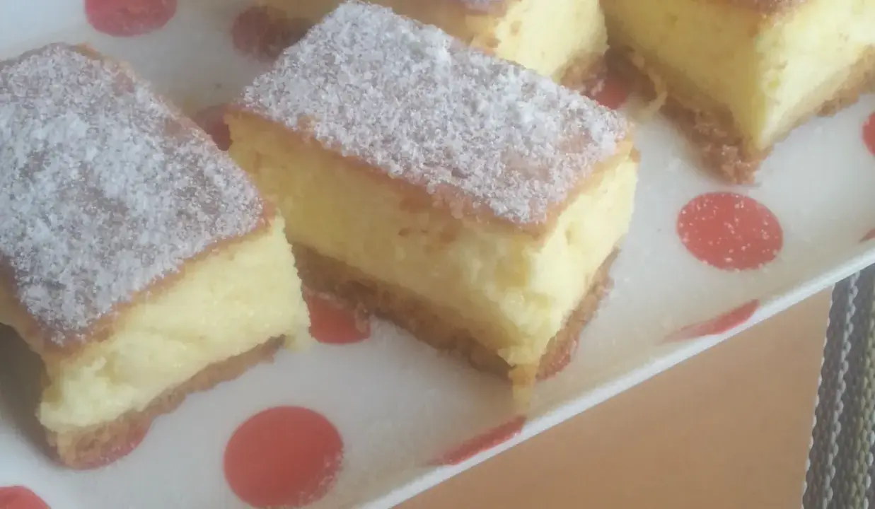 Kawałki puszystego ciasta z kremowym nadzieniem, posypane cukrem pudrem. To zaskakujący sernik bez sera, który zachwyca smakiem.