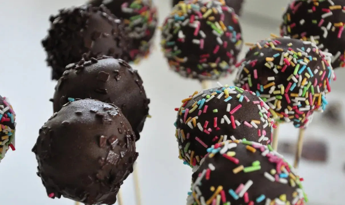 Czekoladowe cake pops na patyczkach, niektóre posypane kolorową posypką. Idealne na imprezę, łatwy cake pops przepis.