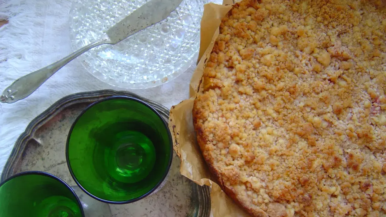 Pyszne kruche ciasto z brzoskwiniami i kruszonką, gotowe do podania z zielonymi kieliszkami.