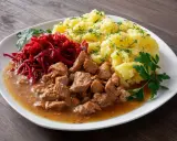 Pyszny gulasz z łopatki wieprzowej z ziemniakami i buraczkami, udekorowany natką pietruszki i koperkiem.