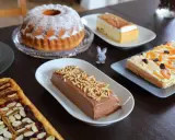 Wielkanocne ciasto na stole: babka, sernik, czekoladowy deser i tartaletka z bakaliami.