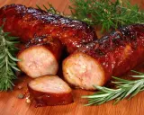 Soczysta kiełbasa z piekarnika, rumiana i aromatyczna, z gałązkami rozmarynu i ziarnami pieprzu na desce.