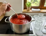 Łyżka nabiera gęsty, gorący przecier pomidorowy z garnka. Obok stoją słoiki, gotowe, by pomieścić ten domowy smak. Tak właśnie przygotowuje się przecier pomidorowy na zimę.