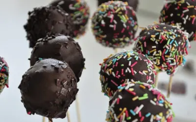 Czekoladowe cake pops na patyczkach, niektóre posypane kolorową posypką. Idealne na imprezę, łatwy cake pops przepis.