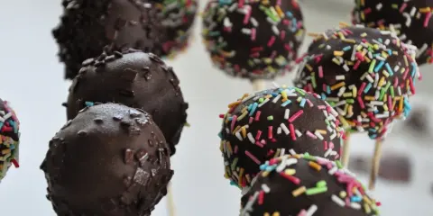 Czekoladowe cake pops na patyczkach, niektóre posypane kolorową posypką. Idealne na imprezę, łatwy cake pops przepis.