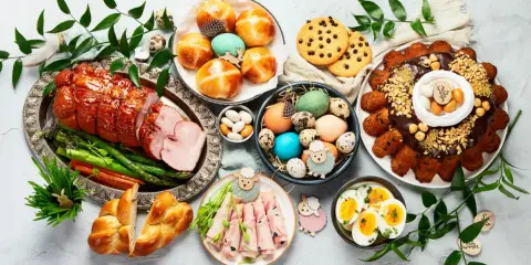 Wielkanocny stół pełen pyszności: pieczona szynka, babki, jajka, ciasto i słodkości.
