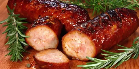 Soczysta kiełbasa z piekarnika, rumiana i aromatyczna, z gałązkami rozmarynu i ziarnami pieprzu na desce.