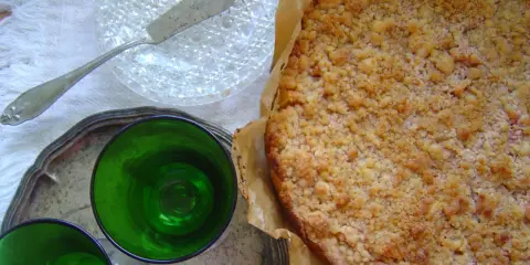 Pyszne kruche ciasto z brzoskwiniami i kruszonką, gotowe do podania z zielonymi kieliszkami.