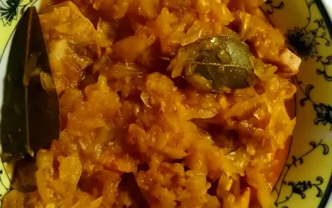 Pyszny bigos ze słodkiej kapusty z liściem laurowym, podany w żółtej misce z czarnym wzorem.