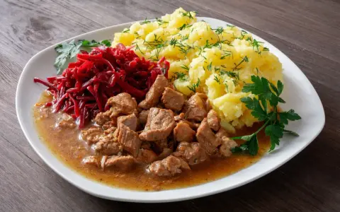 Pyszny gulasz z łopatki wieprzowej z ziemniakami i buraczkami, udekorowany natką pietruszki i koperkiem.
