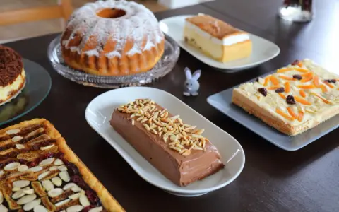 Wielkanocne ciasto na stole: babka, sernik, czekoladowy deser i tartaletka z bakaliami.