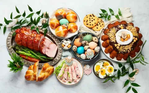 Wielkanocny stół pełen pyszności: pieczona szynka, babki, jajka, ciasto i słodkości.