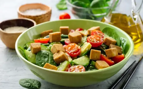 Pyszna sałatka z tofu, pomidorkami koktajlowymi i ogórkiem, posypana sezamem. Idealna na lekki posiłek.