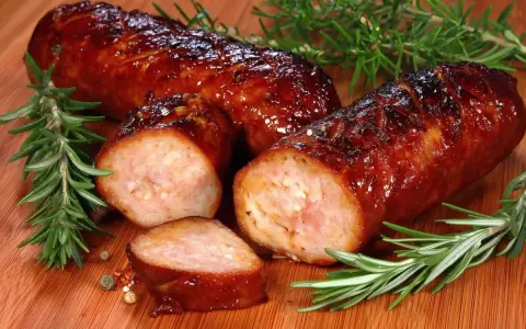 Soczysta kiełbasa z piekarnika, rumiana i aromatyczna, z gałązkami rozmarynu i ziarnami pieprzu na desce.