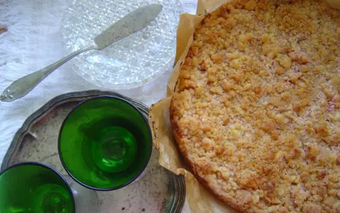 Pyszne kruche ciasto z brzoskwiniami i kruszonką, gotowe do podania z zielonymi kieliszkami.