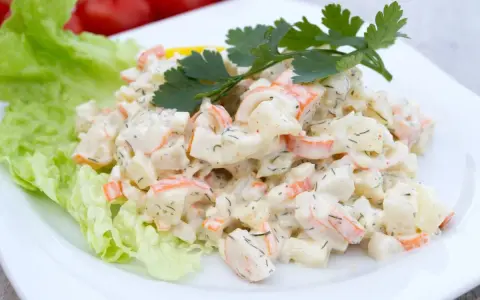 Pyszna sałatka z surimi, ziemniaków i warzyw, udekorowana natką pietruszki i liściem sałaty.