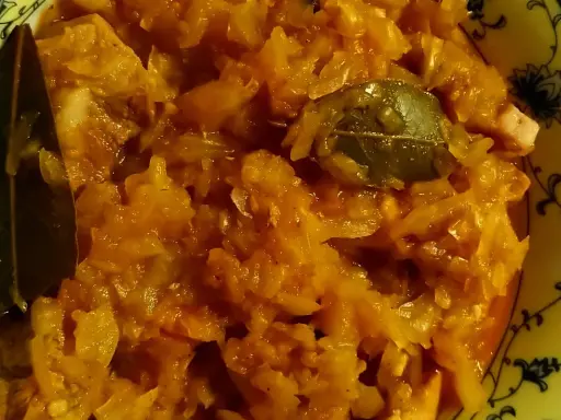 Pyszny bigos ze słodkiej kapusty z liściem laurowym, podany w żółtej misce z czarnym wzorem.