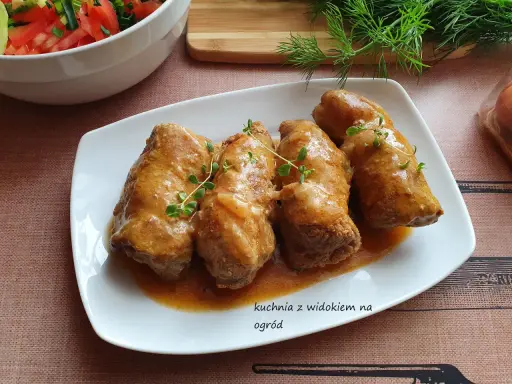 Roladki z karkówki w sosie, udekorowane gałązkami tymianku, obok miski z sałatką.
