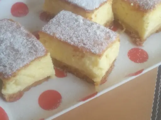 Kawałki puszystego ciasta z kremowym nadzieniem, posypane cukrem pudrem. To zaskakujący sernik bez sera, który zachwyca smakiem.