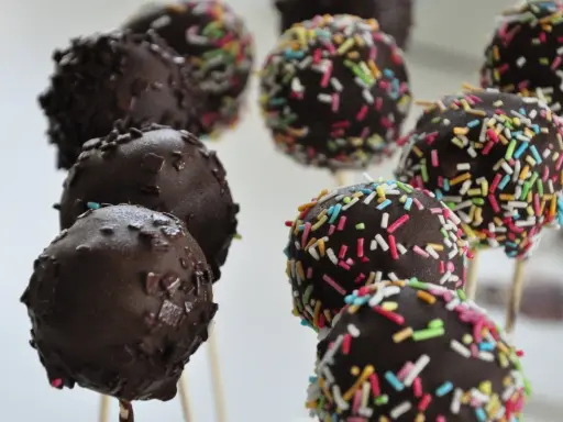 Czekoladowe cake pops na patyczkach, niektóre posypane kolorową posypką. Idealne na imprezę, łatwy cake pops przepis.