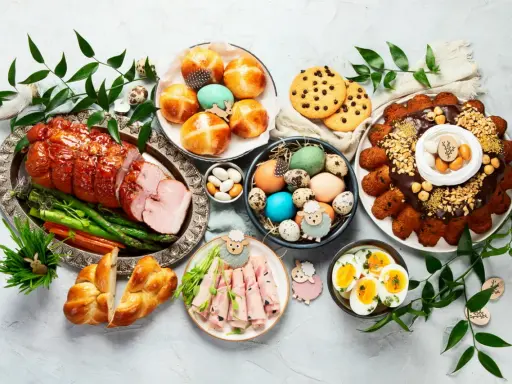 Wielkanocny stół pełen pyszności: pieczona szynka, babki, jajka, ciasto i słodkości.