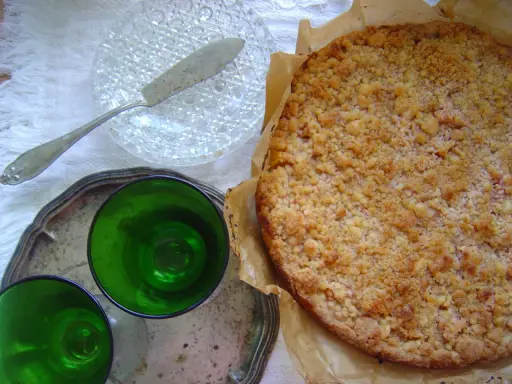 Pyszne kruche ciasto z brzoskwiniami i kruszonką, gotowe do podania z zielonymi kieliszkami.