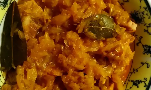 Pyszny bigos ze słodkiej kapusty z liściem laurowym, podany w żółtej misce z czarnym wzorem.