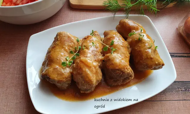 Roladki z karkówki w sosie, udekorowane gałązkami tymianku, obok miski z sałatką.