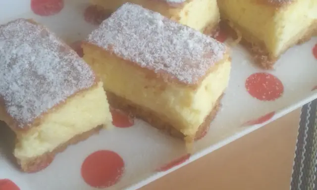 Kawałki puszystego ciasta z kremowym nadzieniem, posypane cukrem pudrem. To zaskakujący sernik bez sera, który zachwyca smakiem.