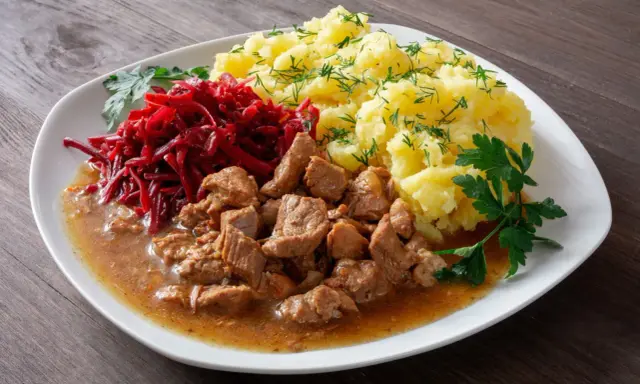 Pyszny gulasz z łopatki wieprzowej z ziemniakami i buraczkami, udekorowany natką pietruszki i koperkiem.