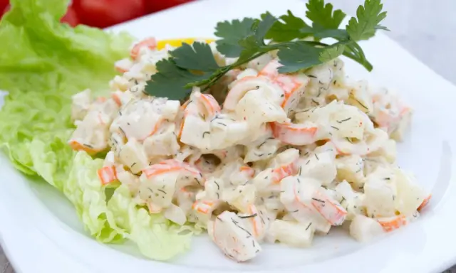 Pyszna sałatka z surimi, ziemniaków i warzyw, udekorowana natką pietruszki i liściem sałaty.