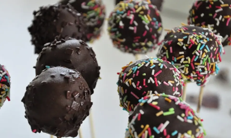 Czekoladowe cake pops na patyczkach, niektóre posypane kolorową posypką. Idealne na imprezę, łatwy cake pops przepis.