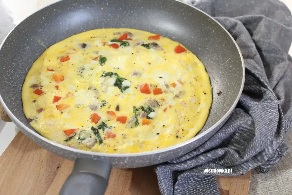 Słony omlet z warzywami, w tym papryką i szpinakiem, smaży się na patelni.