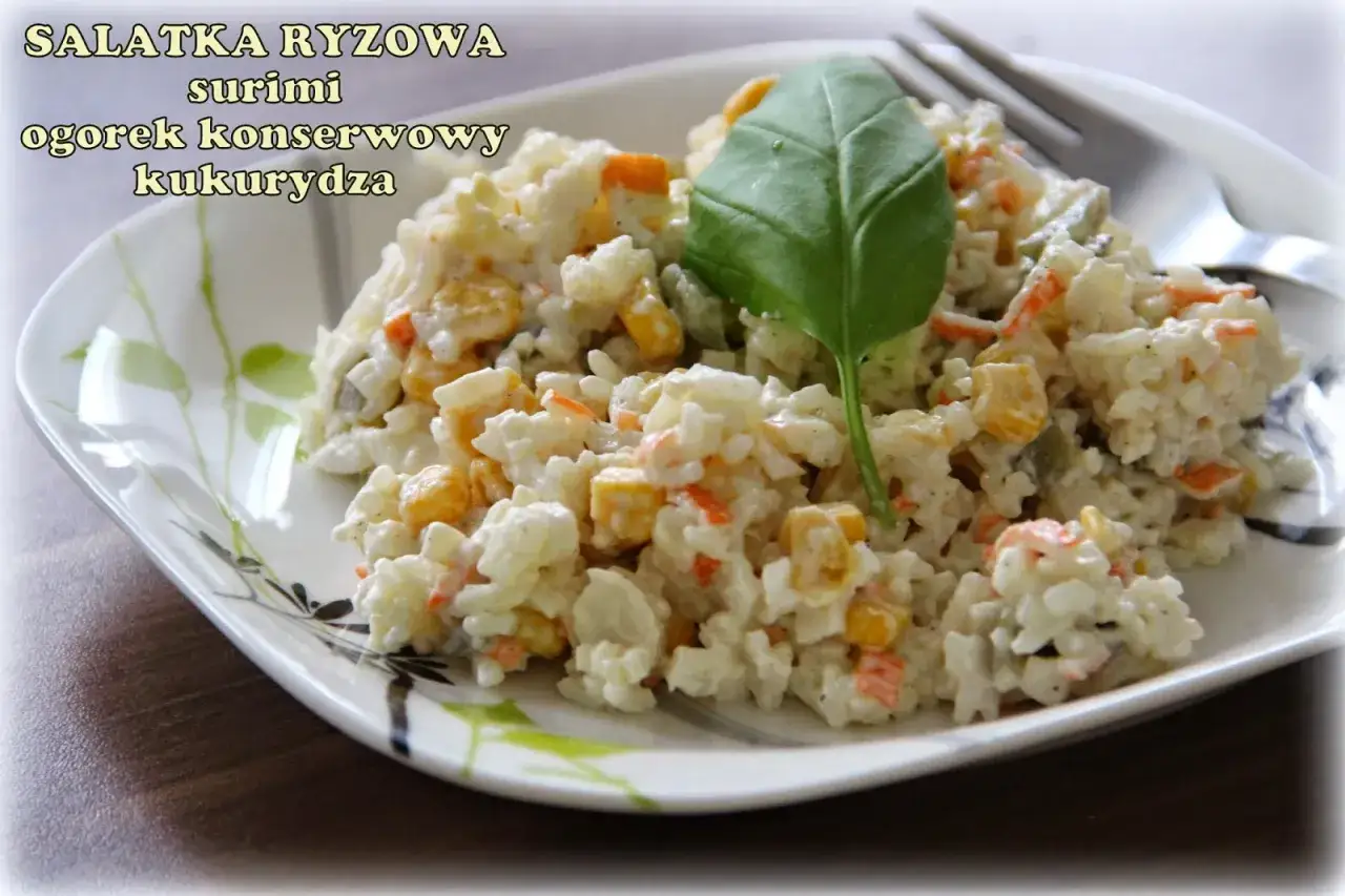 Pyszna sałatka z surimi, ryżu, kukurydzy i og&oacute;rka konserwowego, udekorowana listkiem bazylii.
