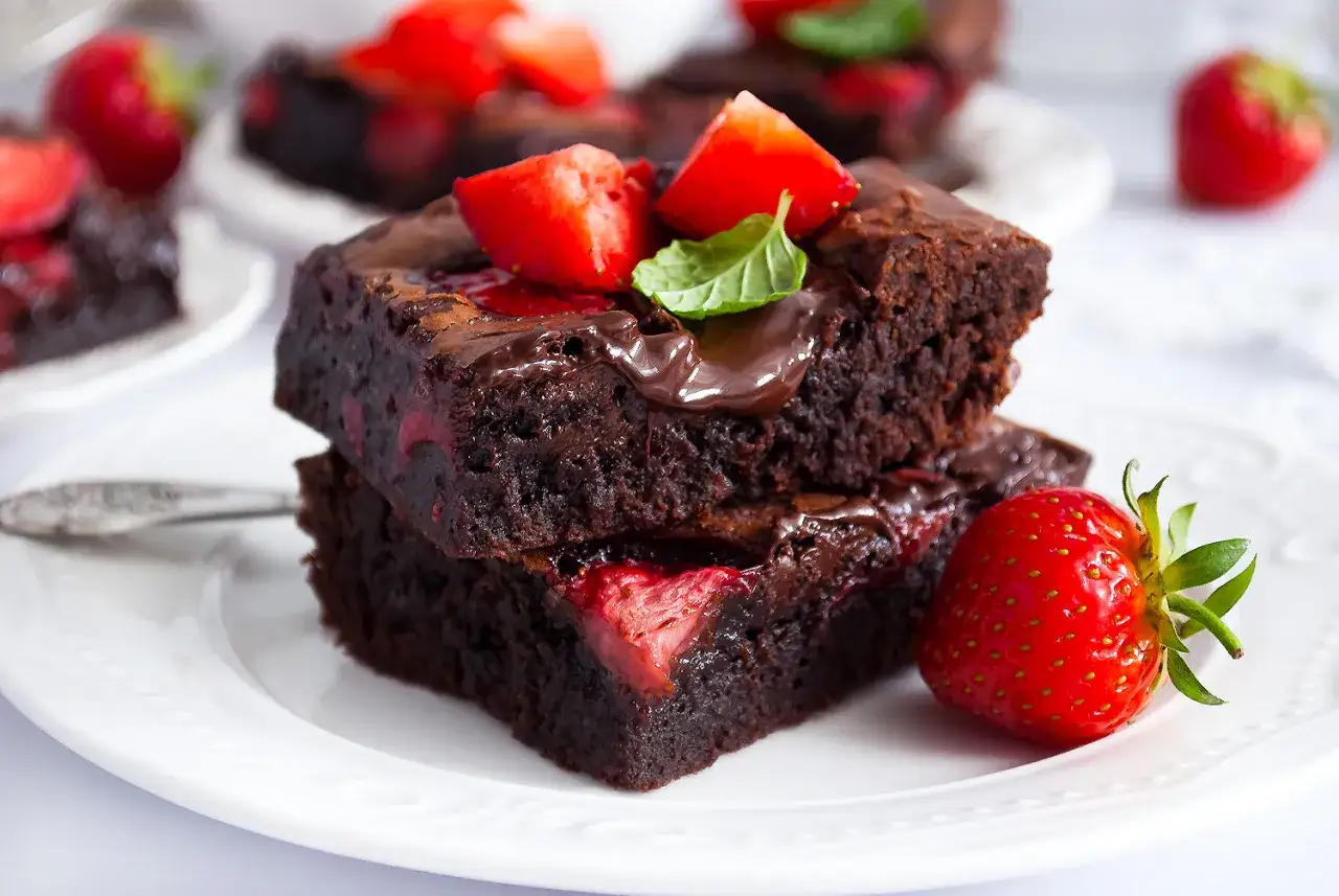 Pyszne brownie z truskawkami, polane czekoladą i ozdobione listkiem mięty. Idealny deser dla każdego łasucha.