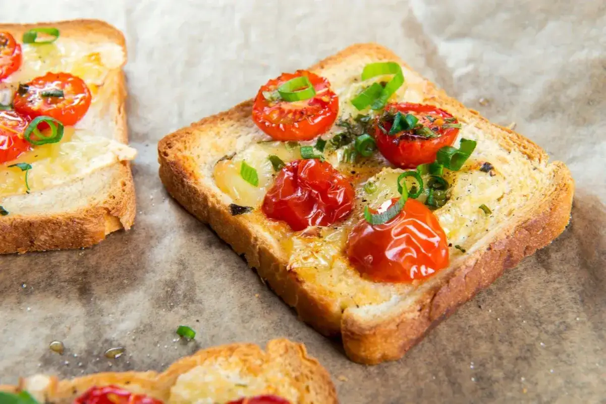 Pyszny pomysł na kolację na szybko: tosty z roztopionym serem, pieczonymi pomidorkami koktajlowymi i szczypiorkiem.
