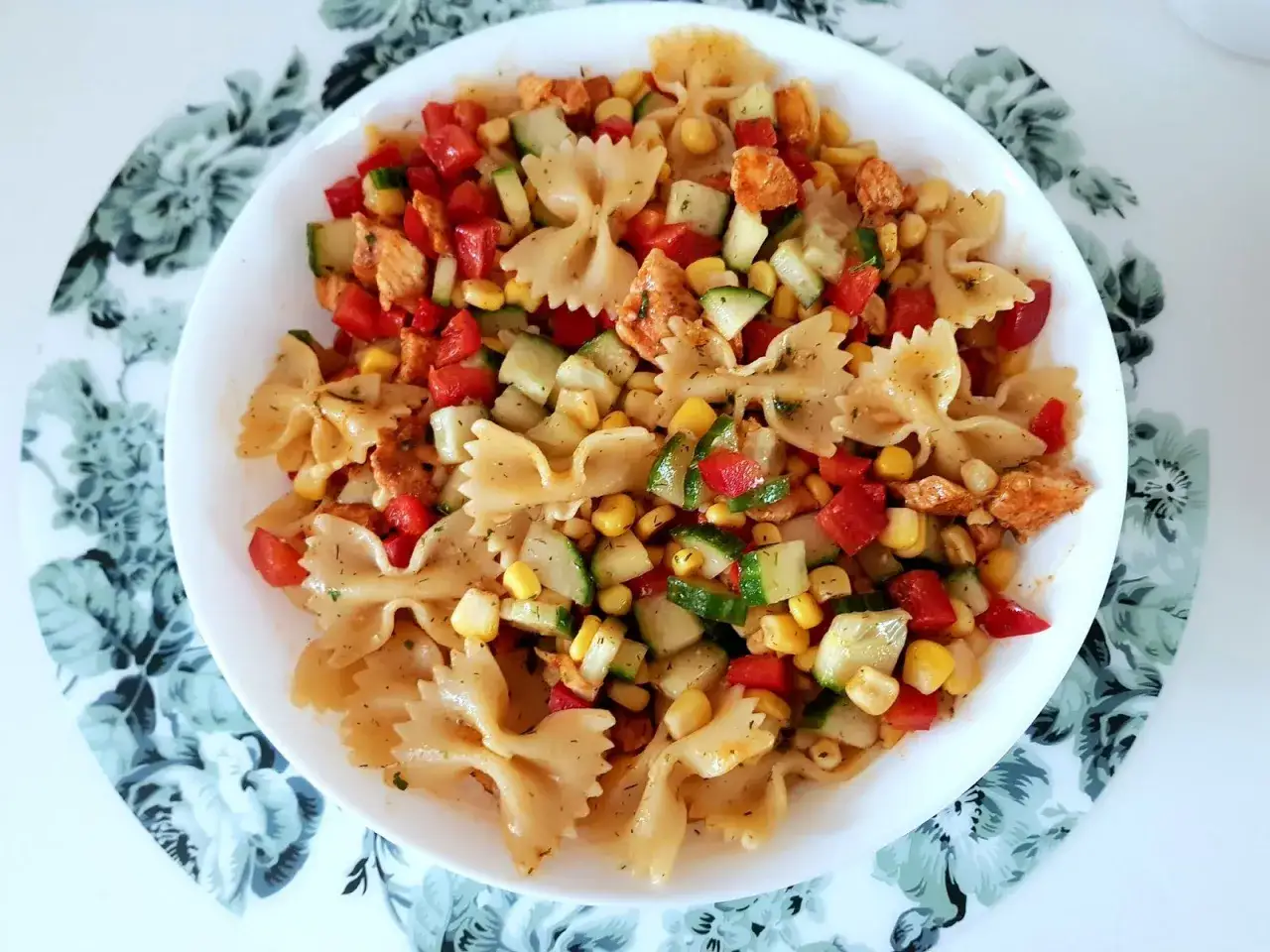 Kolorowa sałatka z makaronem farfalle, kurczakiem, kukurydzą, pomidorkami i ogórkiem. Pyszne danie na lato.